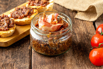 Smoked bacon jam in a glass jar on a wooden table.