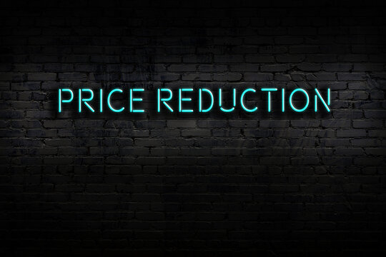 Neon sign. Word price reduction against brick wall. Night view