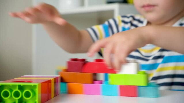 A boy of 5 years old plays as a constructor, builds from multi-colored cubes