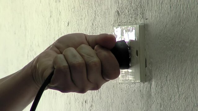 Male Hand Connecting Three Pin Plug Into Wall Socket. Close Up.  