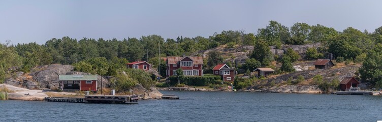 Fototapeta na wymiar Panorama view, commuting boat jetty, island Södra Stavsudda, summer houses on smooth cliffs, jetties and boats at an open bay in the archipelago a sunny summer day in Stockholm