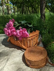 Wooden basket and bag with flowers on summer picnic with green grass on background.