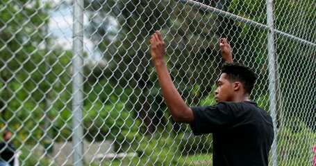 African black man leaning on metal fence outside watching game