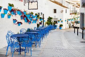 Row of blue cafe tables and chairs with potted plants in the town of Mijas, Pueblo Blanco, Spain - obrazy, fototapety, plakaty