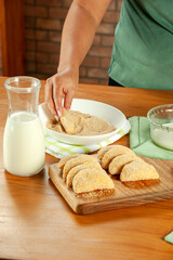 Woman breading brazilian meat stuffed croquette (risolis de carne) on a wooden table. Top view.