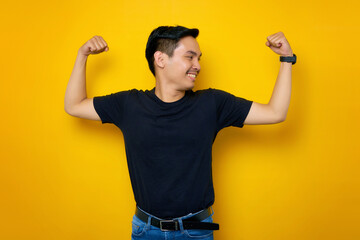 Smiling Asian Muslim man raises arms and showing muscle isolated over Yellow background