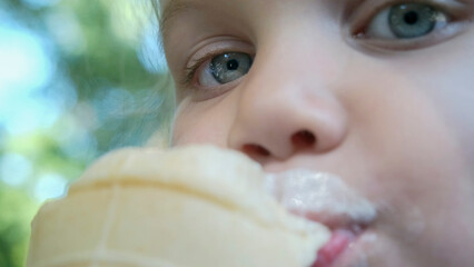 Cute little girl eats ice cream outside. Close-up portrait of blonde girl sitting on park bench and eating icecream.