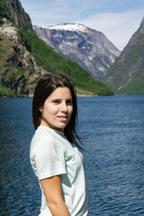 Young tourist girl in the foreground and behind her the fjord with the high mountains in Gudvangen - Norway