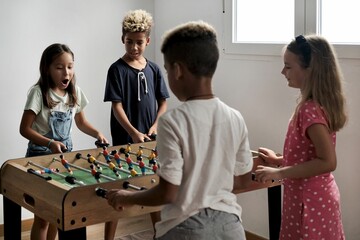 Group of multi-cultural cute children spending playtime with friends playing foosball together.