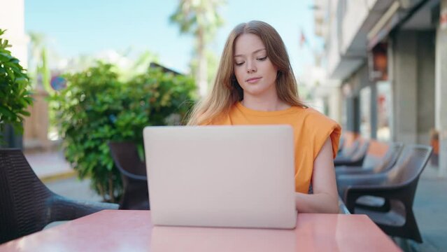 Young woman using laptop sitting on table at coffee shop terrace