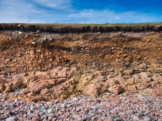 Eroding soil, subsoil and bedrock at a pebble beach near Sand Wick and Hillswick in Northmavine, Shetland, UK. Taken on a sunny day with a blue sky in the background. - obrazy, fototapety, plakaty