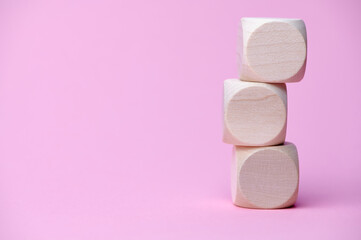 three wooden cubes on each other, copy space for any text, pink background paper