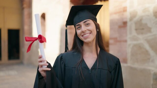 Young hispanic woman wearing graduated uniform pointing with finger to diploma at university
