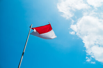 Red and white The national flag of the country of Indonesia on a bright blue sky background with white clouds