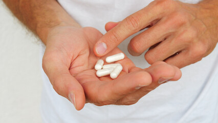 Close-up of a man's hand holding medicine capsules and about to take them