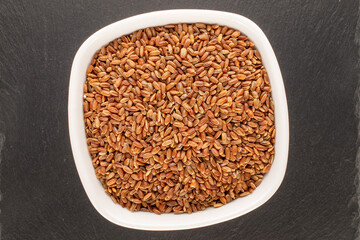 Organic uncooked brown rice in a ceramic plate on a slate stone, close-up, top view.