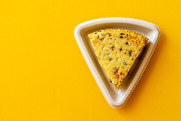 Portion of Spanish omelette, in a recycled cardboard container, on a yellow background