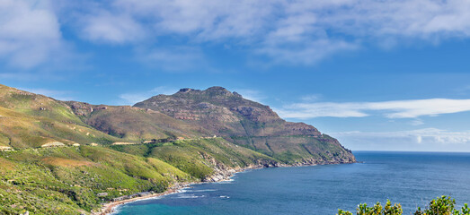 A landscape of a mountainside with an ocean view and blue sky background with a lush, green...