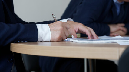 Man in an elegant suit signs or endorses a document during a working meeting or negotiations. No...