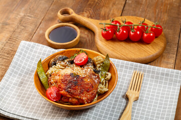 Udon with vegetables and chicken with sesame seeds in a wooden plate next to tomatoes and champignons and soy sauce on a plank.