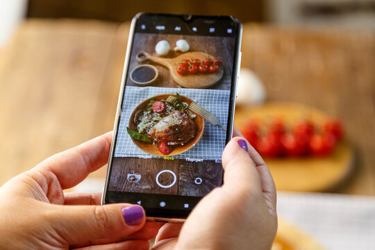 Udon with vegetables and chicken with sesame seeds in a wooden plate woman takes a picture with a smartphone.