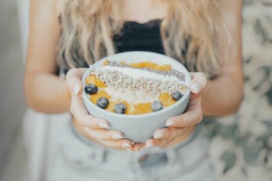 Selective focus shot of a woman's hands holding a smoothie bowl with blueberries and seeds
