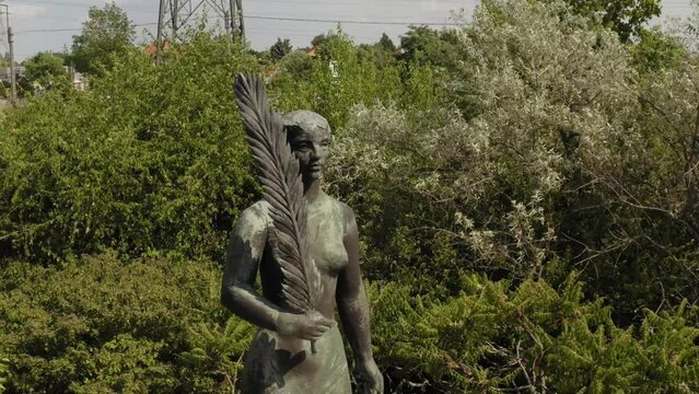 Closeup of a statue of a female holding a feather in one hand surrounded by greenery