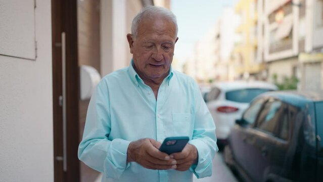 Senior grey-haired man using smartphone at street