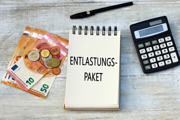Das deutsche Wort Entlastungspaket auf einem Notizblock mit Geldscheinen und Taschenrechner.