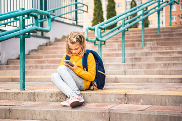 Back to elementary, primary school. Little girl with backpack,mobile phone. Chat, talk with friends, classmates on break. Autumn study after vacation. Education of children. Pupil kid on stair steps