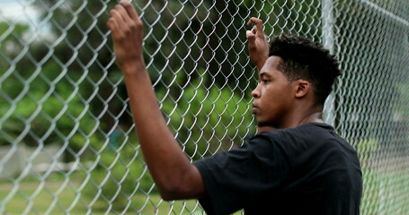 Pensive young black man leaning on metal fence. Contemplative mixed race person