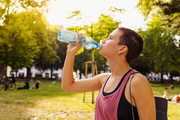 athletic teenage drinks sports isotonic from bottle after sports training, yoga, ina public park, sunset. Healthy lifestyle, sports, outdoor fitness. Useful training, athletic physique, strong muscles