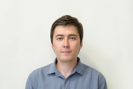 Young Attractive Man, Close-up Face In A Blue Shirt On A White Background Copy Space. Portrait Of A Positive Young Man