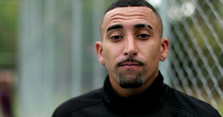 Pensive hispanic man leaning on metal fence looking at camera. Latin guy portrait