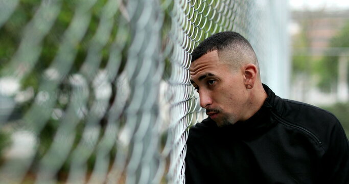 Pensive hispanic man leaning on metal fence looking at camera. Latin guy portrait