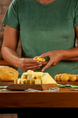Cheese cubes with woman preparing brazilian croquettes stuffed with cheese in background.