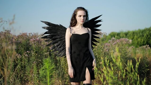 Goddess of death and bloody revenge in the field posing for a photo. Fallen black angel with black wings. Halloween concept.