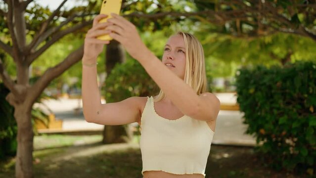 Young blonde woman smiling confident making photo by the smartphone at park