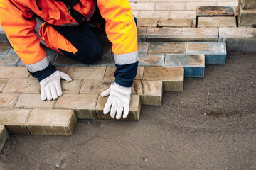 a worker in a protective work suit lays paving slabs. A professional