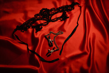 Black mask and nipple clamps on a red background. Love games. Games for adults. soft focus