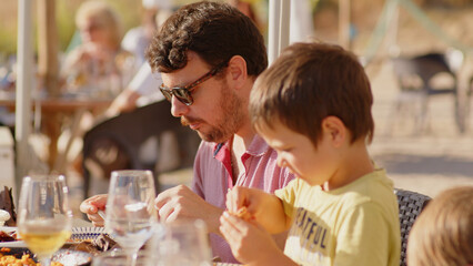 Family and friends gathered for lunch enjoying a delicious paella in a bar on the beach - happy little kids playing around the table after eating, eating dessert and ice cream