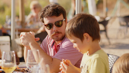 Family and friends gathered for lunch enjoying a delicious paella in a bar on the beach - happy little kids playing around the table after eating, eating dessert and ice cream