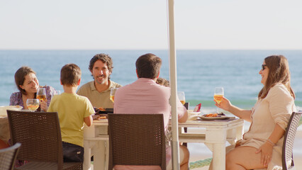Family and friends gathered for lunch enjoying a delicious paella in a bar on the beach - happy little kids playing around the table after eating, eating dessert and ice cream