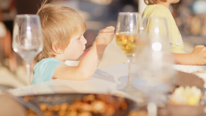 Family and friends gathered for lunch enjoying a delicious paella in a bar on the beach - happy little kids playing around the table after eating, eating dessert and ice cream