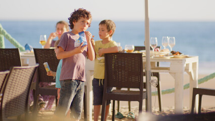 4 sibling boys look at the camera smiling, play while running through a restaurant in front of the camera, eat ice cream, hug their mother