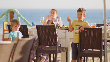 4 sibling boys look at the camera smiling, play while running through a restaurant in front of the camera, eat ice cream, hug their mother