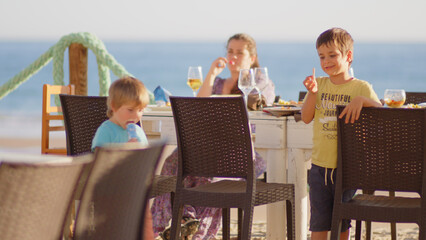 4 sibling boys look at the camera smiling, play while running through a restaurant in front of the camera, eat ice cream, hug their mother