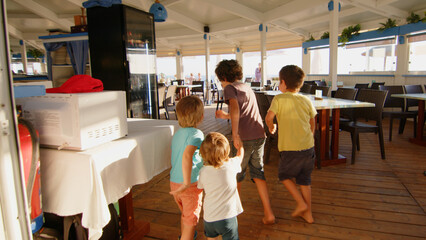 4 sibling boys look at the camera smiling, play while running through a restaurant in front of the camera, eat ice cream, hug their mother