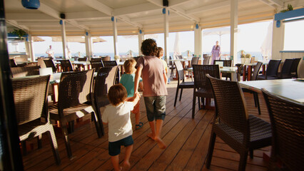 4 sibling boys look at the camera smiling, play while running through a restaurant in front of the camera, eat ice cream, hug their mother