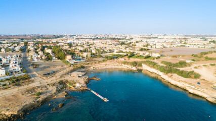 Fototapeta premium Aerial bird's eye view of Kapparis beach, Protaras, Paralimni, Famagusta, Cyprus. Famous tourist attraction Kaparis bay with boats, sunbeds, restaurant, water sports, people swimming in sea from above